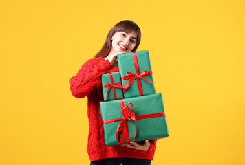 Fototapeta premium Smiling woman in red sweater with many gift boxes on yellow background. Christmas and New Year celebration
