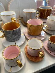 Ceramic teacups with gold accents on saucers displayed in a light-filled setting