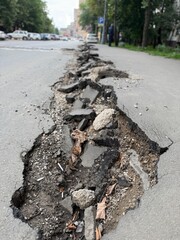 Damaged urban road with large crack showing broken asphalt and exposed dirt with leaves