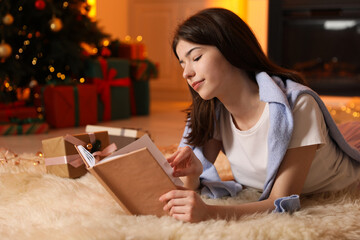 Naklejka premium Beautiful woman reading book on floor in room decorated for Christmas