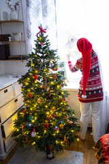 A woman in a Santa hat hangs curtains in the bedroom on the skylights with a Christmas tree and...