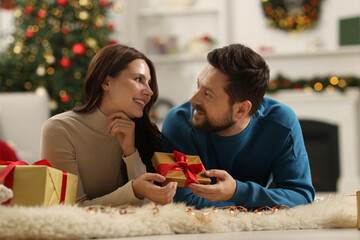 Happy couple with gift box spending time together in room decorated for Christmas