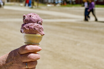 Close up view of a person outdoors, holding a cone with cherry ice cream