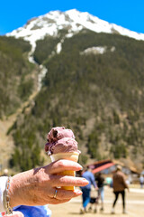 Close up view of a person on holiday holding a cone with cherry ice cream with a snow capped mountain in the background
