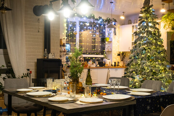 Festive interior of house is decorated for Christmas and New Year in loft style with black stove, fireplace, Christmas tree. Warm studio room with set table, burning wood, cozy and heating of home