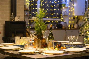 Festive interior of house is decorated for Christmas and New Year in loft style with black stove, fireplace, Christmas tree. Warm studio room with set table, burning wood, cozy and heating of home