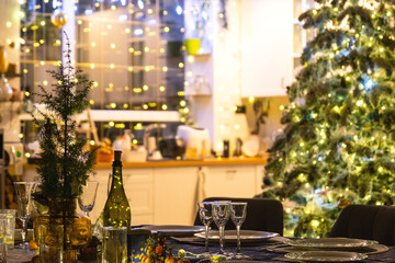 A festive table set for guests for Christmas and New Year, a Christmas tree in the living room, plates, bottles, glasses, potted plants, fairy lights
