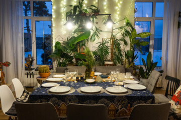 A festive table set for guests for Christmas and New Year, in the living room, plates, bottles, glasses, potted plants, fairy lights