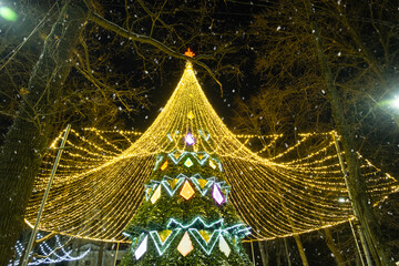 High city Christmas tree with a mushroom cap made of garlands, glows at night on the street. Christmas, New Year, decoration of the city. 