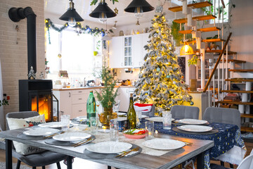 Festive interior of house is decorated for Christmas and New Year in loft style with black stove, fireplace, Christmas tree. Warm studio room with set table, burning wood, cozy and heating of home