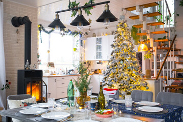 Festive interior of house is decorated for Christmas and New Year in loft style with black stove, fireplace, Christmas tree. Warm studio room with set table, burning wood, cozy and heating of home