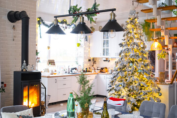 Festive interior of house is decorated for Christmas and New Year in loft style with black stove, fireplace, Christmas tree. Warm studio room with set table, burning wood, cozy and heating of home