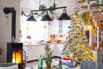 Festive interior of house is decorated for Christmas and New Year in loft style with black stove, fireplace, Christmas tree. Warm studio room with set table, burning wood, cozy and heating of home