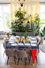 A festive table set for guests for Christmas and New Year, in the living room, plates, bottles, glasses, potted plants, fairy lights
