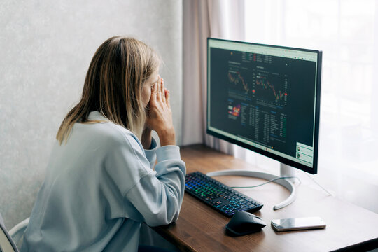 Middle-aged woman stressed at computer screen reviewing investment charts and market data
