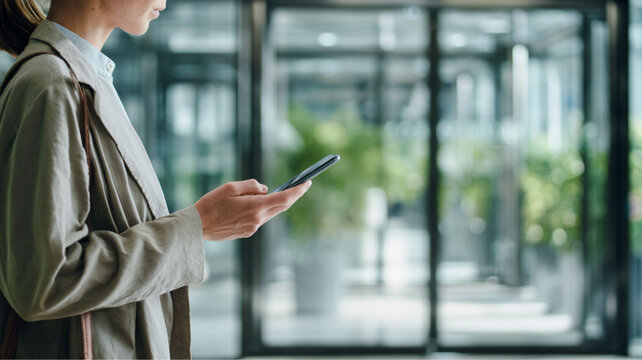 Young Asian Woman Using Smartphone in Modern Office Lobby with Glass Doors and Natural Light