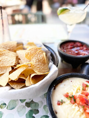 Delicious tortilla chips and salsa served with cheesy dip and a refreshing cocktail outdoors at a restaurant