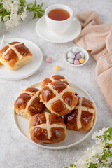 Traditional Easter hot cross buns on a white plate with butter, berry jam and cup of tea. Delicious Easter breakfast.