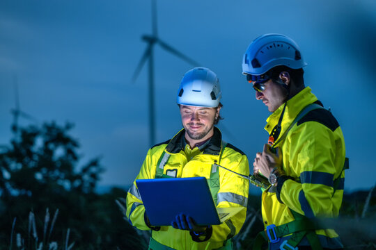 Engineers Team Night Communication Laptop Monitoring Wind Turbine. Night Time Renewable Energy Management Communication Device. Industrial Professionals Evening Inspection Communication