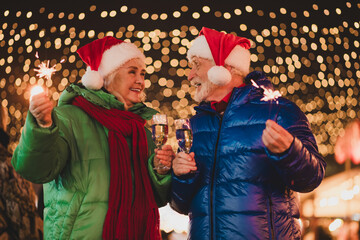 Funny couple celebrate Christmas together with sparklers and champagne under twinkling lights at a...