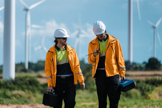 Professional Technicians Discussing Renewable Power Operation, Talking Walking Wind Turbine Background. Reporting Wind Turbine Status. Future Grid Development Team Discussing Field Inspection