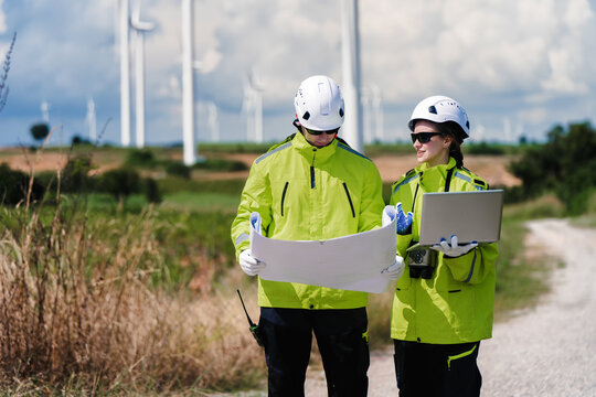 Engineers Planning with Blueprint and Digital Technology at Wind Turbine Site. Clean Energy Professionals Analyzing Site Plan Documentation. Collaboration Documentation Wind Power Design.