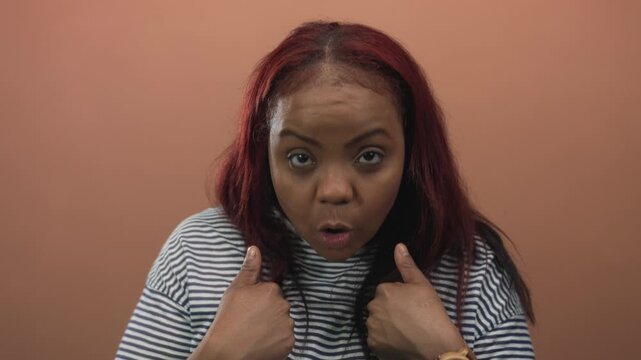 African american woman points finger to herself with astonished expression in a studio setting; surprise.