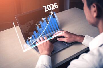 A businessman analyzes future growth projections on his laptop. A digital graph outlines significant market trends for 2026, emphasizing strategic planning in business. Tessel