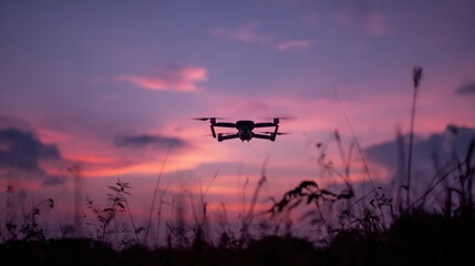 Drone silhouetted against a vibrant pink and purple sunset with tall grass