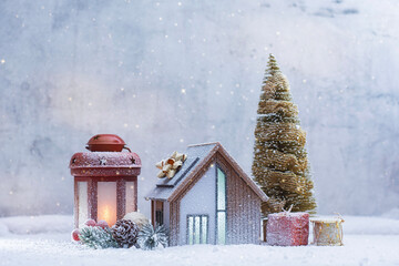 Festive winter composition with a miniature house with solar panel, glowing lantern, Christmas tree and gift boxes. Concept holiday atmosphere for Christmas, New Year and winter celebration.