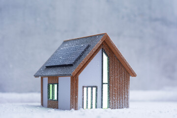 Contemporary eco-friendly house model with solar panels on the roof covered in snow. Concept sustainable energy and smart living during winter.