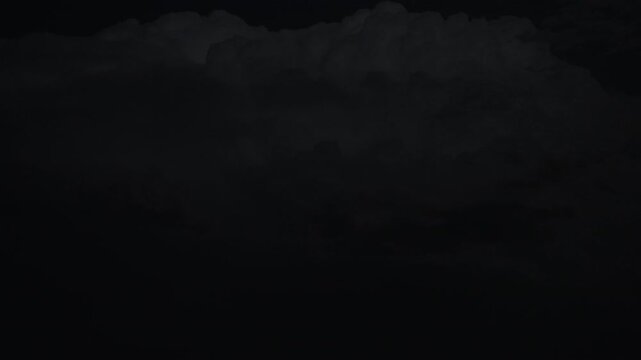 Distant lightning storm glowing through heavy clouds over countryside at night 