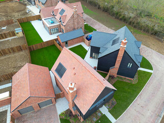 Low level drone view of newly completed detached family homes seen as part of a housing development project in rural Britain. Note the newly laid lush lawns.