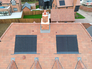 Abstract drone view of a newly completed tiled roof and fitted solar panels seen on a semi detached affordable home within the confines of a rural British housing development site.