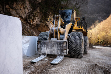 Yellow heavy wheel loader with forks and tire chains at a marble quarry in Greece, parked beside a...
