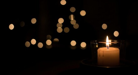 single lit candle in the dark with golden bokeh lights