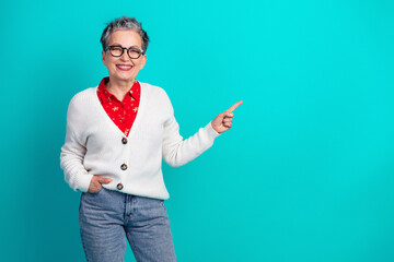 Confident elderly woman in white cardigan red shirt and jeans smiles and points to the right...