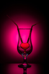 Romantic concept with heart-shaped straw in an empty glass on crimson background – symbol of love, relationship, and togetherness. Minimalistic Valentine’s Day still life.