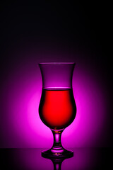 Glass of red drink with vibrant pinnk backlight on reflective surface, minimalistic still life beverage concept.