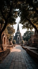 Fototapeta premium An ancient temple ruin in Thailand featuring a large stupa rising prominently in the scene. Weathered brick structures, aged stone textures, and surrounding greenery create a historic vibes