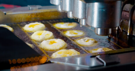 Industrial food processing equipment drops raw dough into hot oil, frying and cooking doughnuts in an automated process