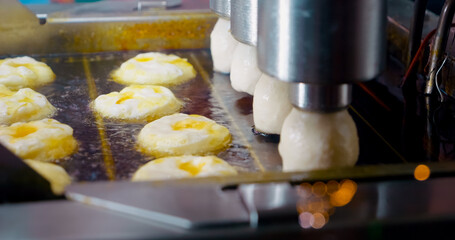 Modern industrial machinery executing systematic doughnut production, systematically deep frying pastries in large scale boiling oil processing line