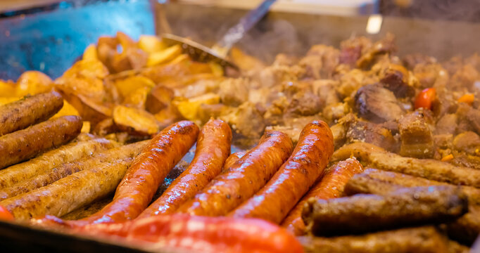 Street food vendor grilling sausages and potatoes on large hot plate, showcasing traditional outdoor culinary experience in bustling urban market setting