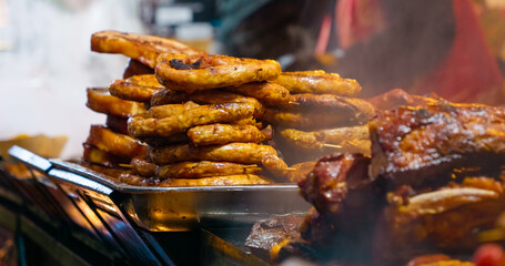 Street food vendor carefully arranging freshly grilled sausages on metal tray at bustling local market stall, highlighting culinary tradition