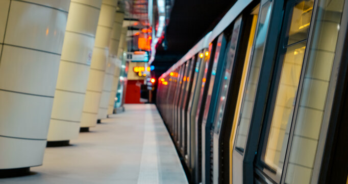 A subway platform captures the hustle of public transport. Doors reflect colorful lights as commuters prepare for their evening travels in the city.