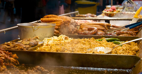 Close up of steaming sausages, sauerkraut, and other street food cooking on a hot plate at a Christmas market