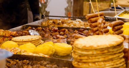 Romanian street food, including polenta, mici, sausages, and pita bread, cooking on a large hot plate