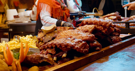 Street food vendor grilling savory barbecue ribs at traditional Christmas market, preparing hot winter meal for hungry visitors