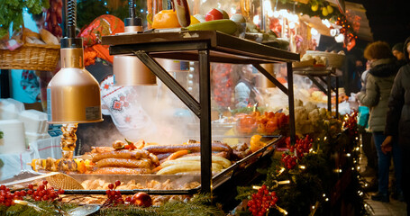 Delicious meats and sausages are showcased at a festive market. The warm lights and seasonal atmosphere invite visitors to taste the holiday delights available.