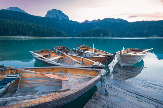 Rowing boats tied to pier on still water lake surrounded by mountains at sunset, Durmitor, Montenegro